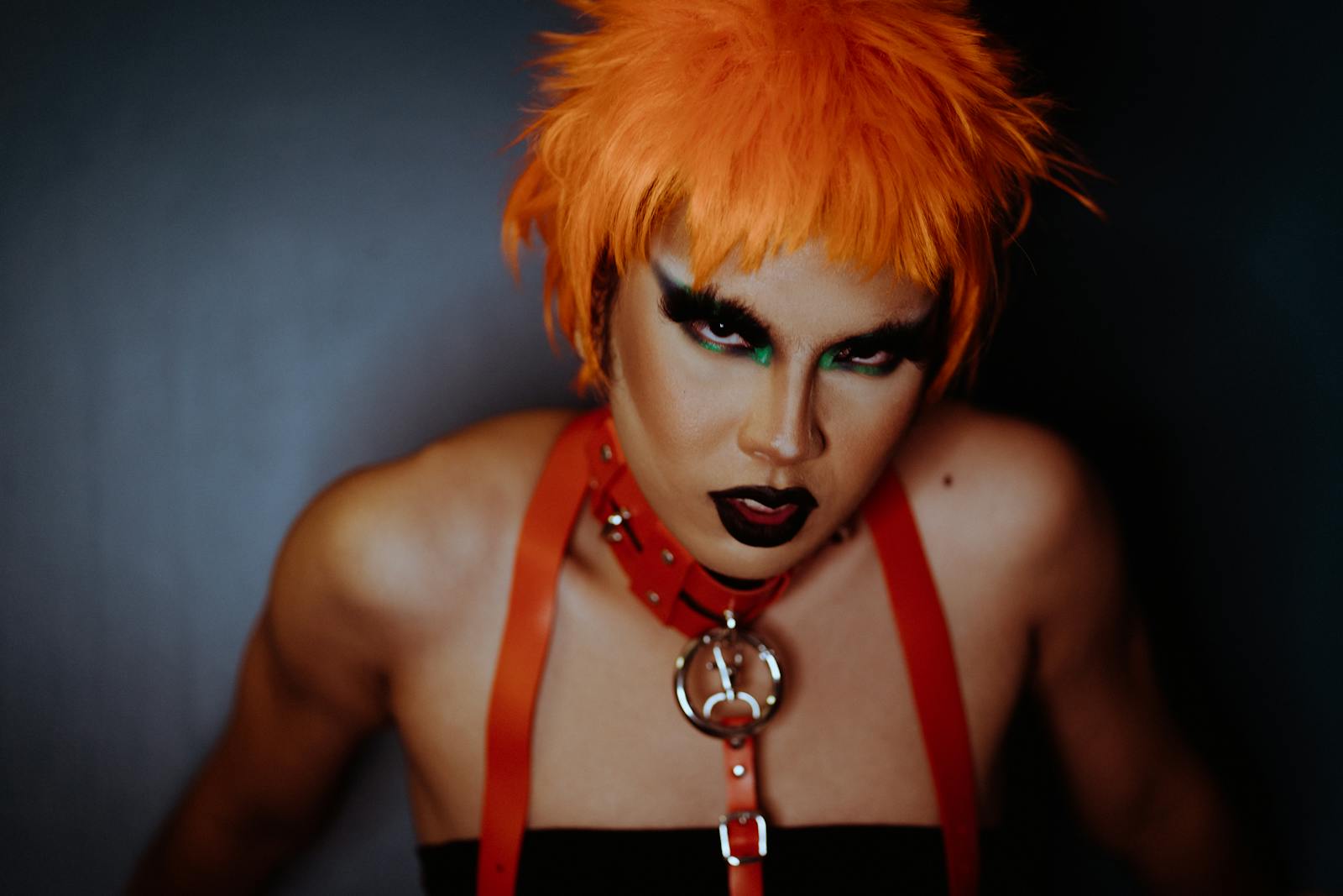 Striking portrait of a model with vibrant orange hair and dramatic makeup in a creative studio setting.